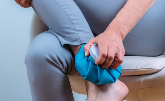 Ankle pain treatment. Senior woman holding ice bag compress on a painful ankle joint.