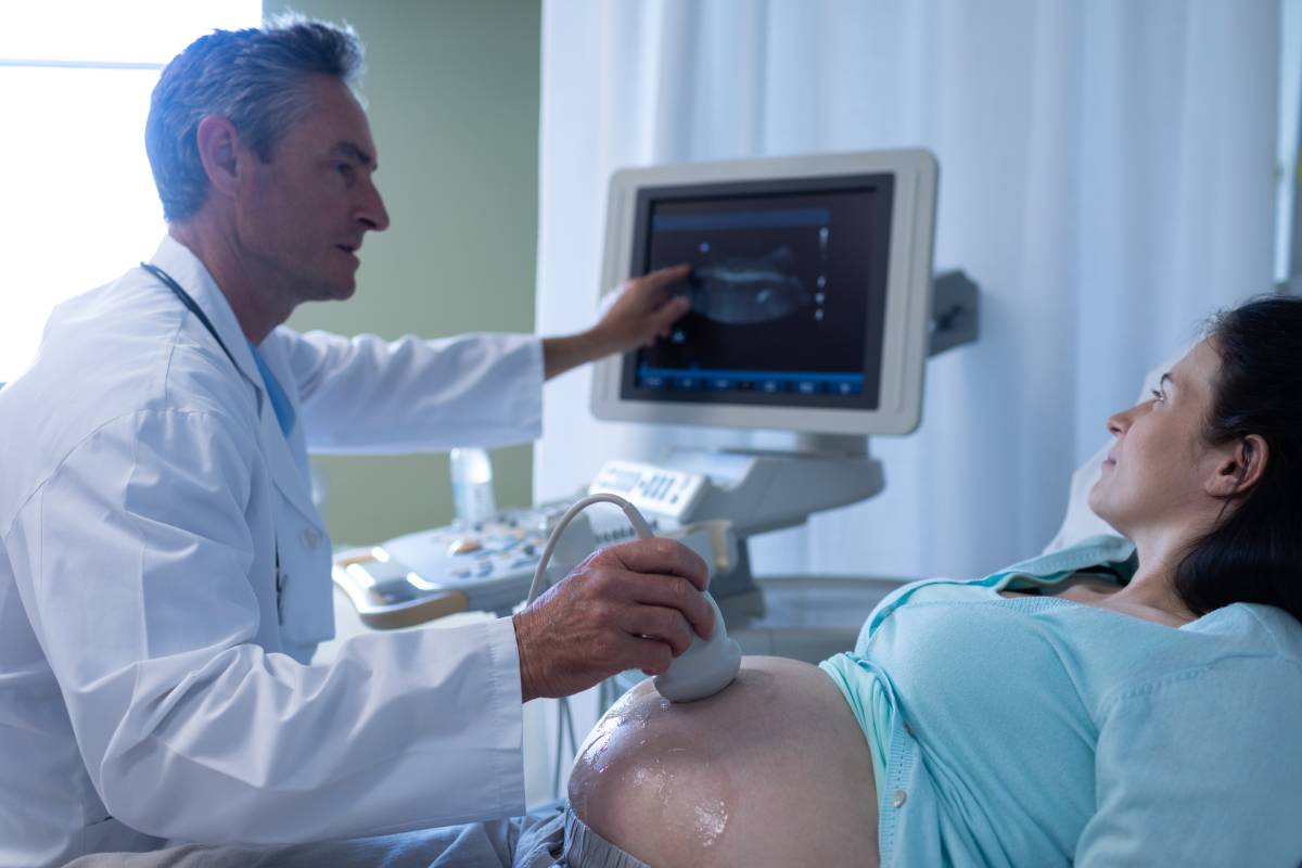 Side view of Caucasian male doctor doing ultrasound scan for pregnant woman in hospital