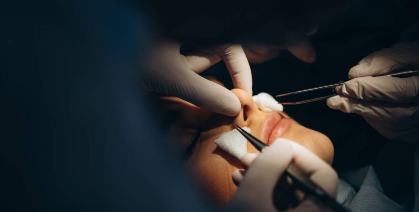 Surgeon and his assistant performing cosmetic surgery on nose in hospital operating room. Nose reshaping, augmentation. Rhinoplasty.
