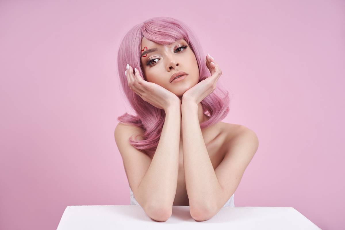 Romantic Woman with dyed pink strong hair at table on pink background. Natural colored hair beautiful makeup, strong roots
