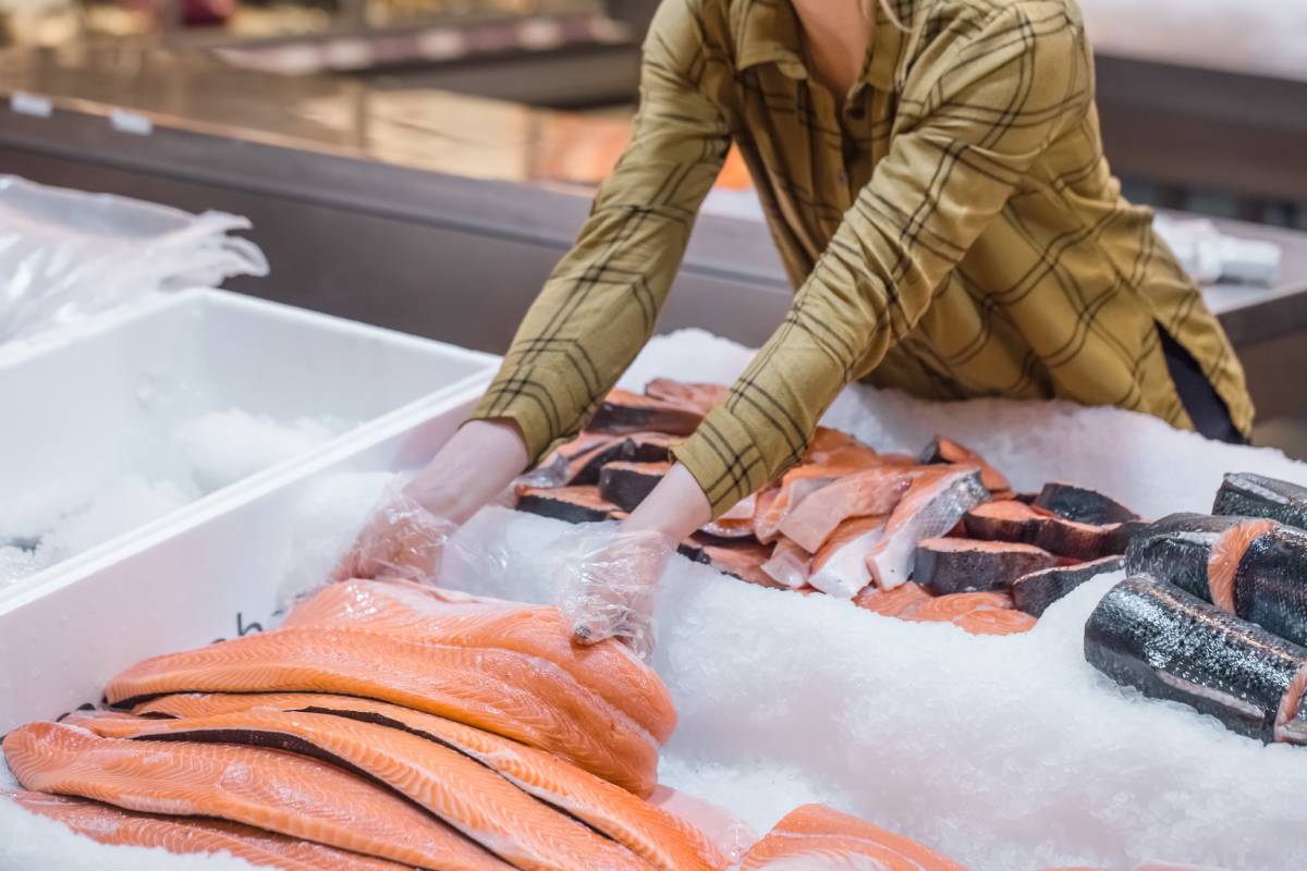 Woman in the supermarket. Beautiful young woman holding a salmon fish in her hands.